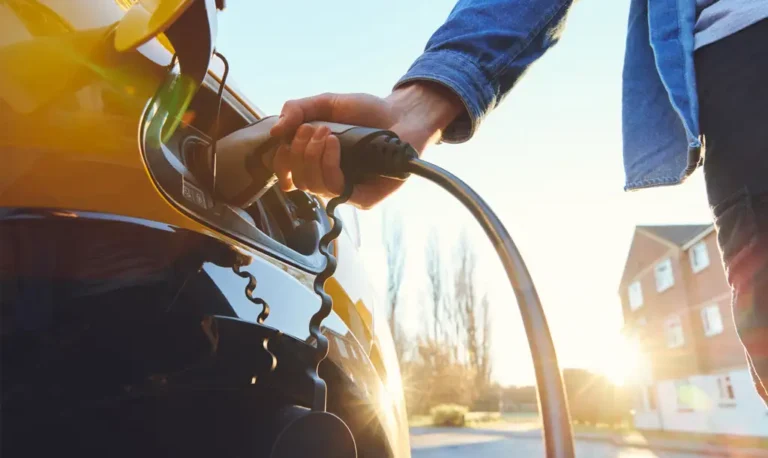 STREL : Main branchant une prise de recharge électrique dans une voiture blanche, devant une borne de recharge extérieure entourée de verdure, illustrant la recharge facile et écologique en France